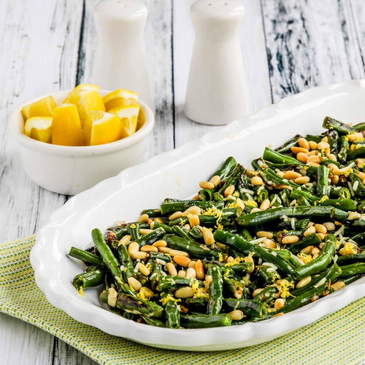 Green Beans with Lemon, Parmesan, and Pine Nuts shown on serving platter with lemons in back.