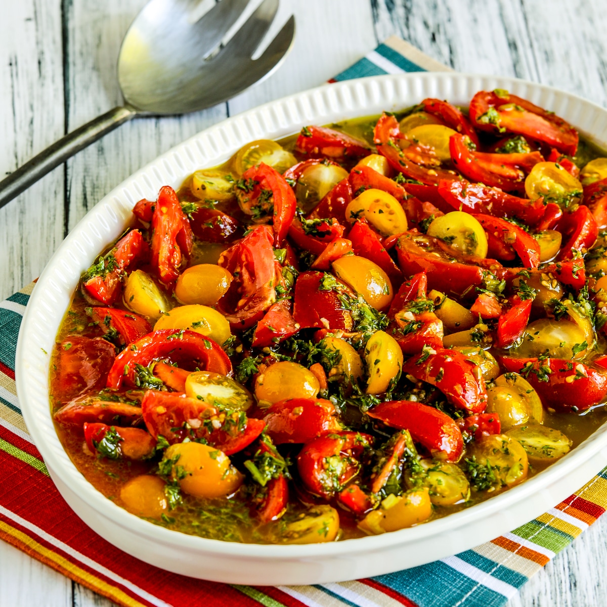 marinated tomatoes on serving dish with fork and colorful striped napkin