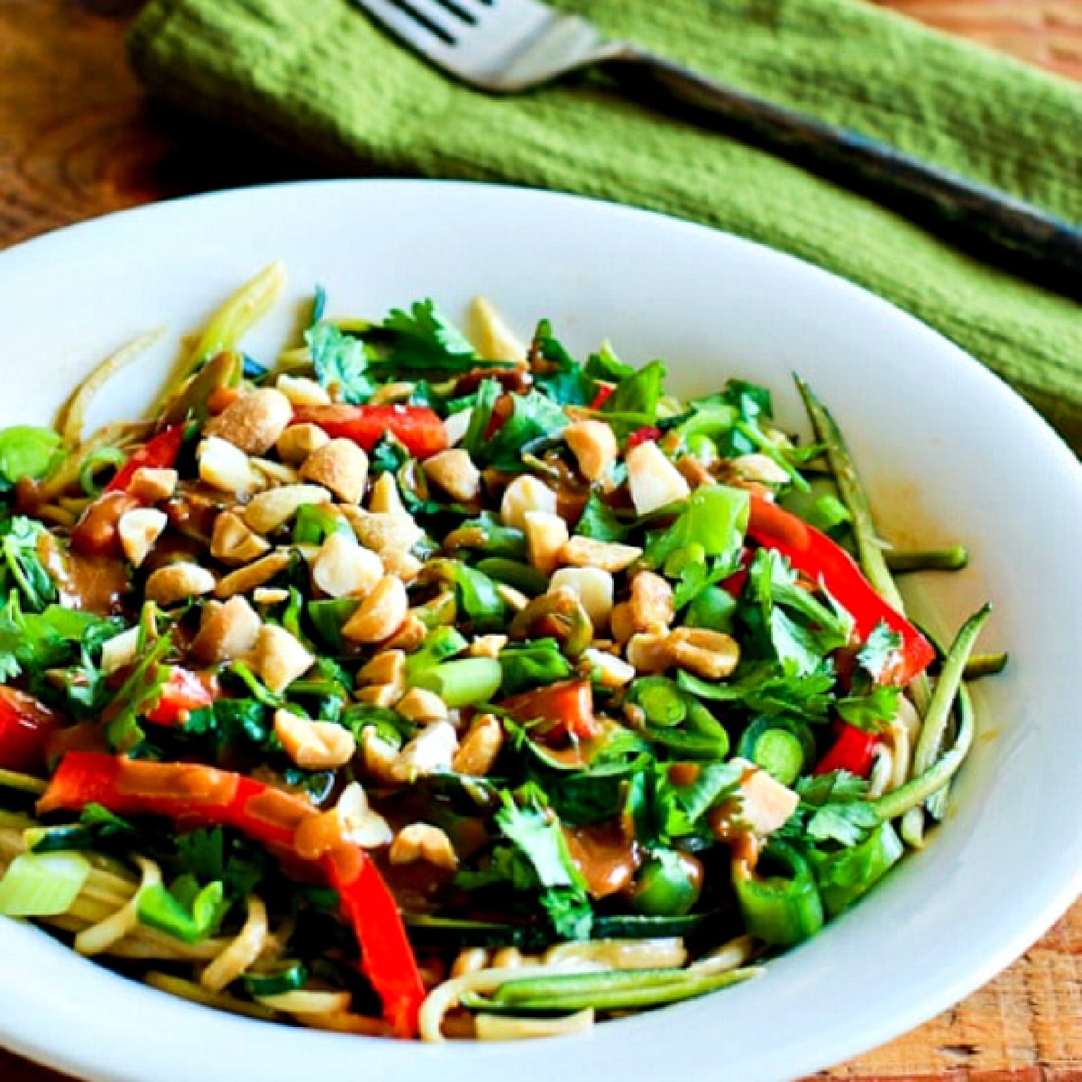 Zucchini Noodle Bowl with Peanut Sauce on wood table with green napkin