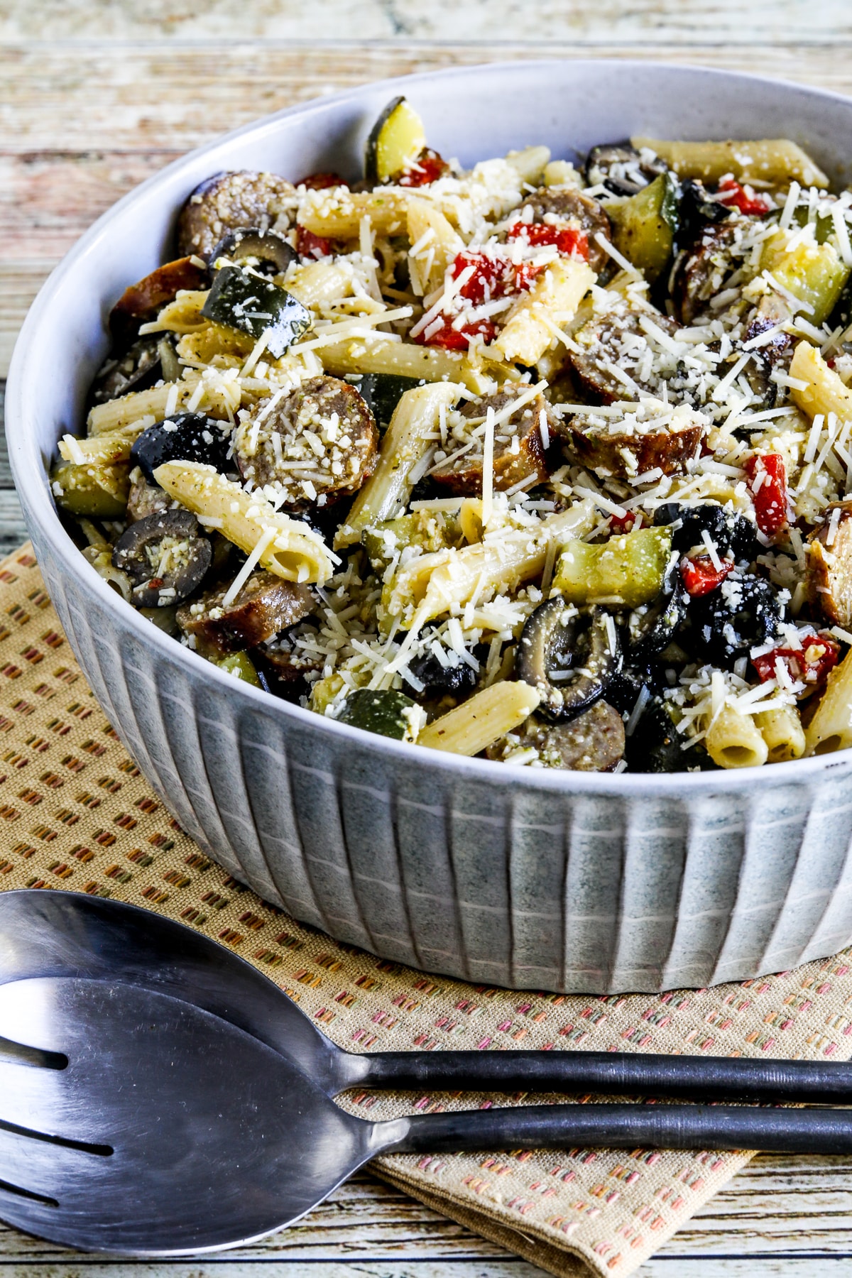 Pasta Salad with Sausage, Zucchini, Olives, and Peppers shown in serving bowl with forks and napkin