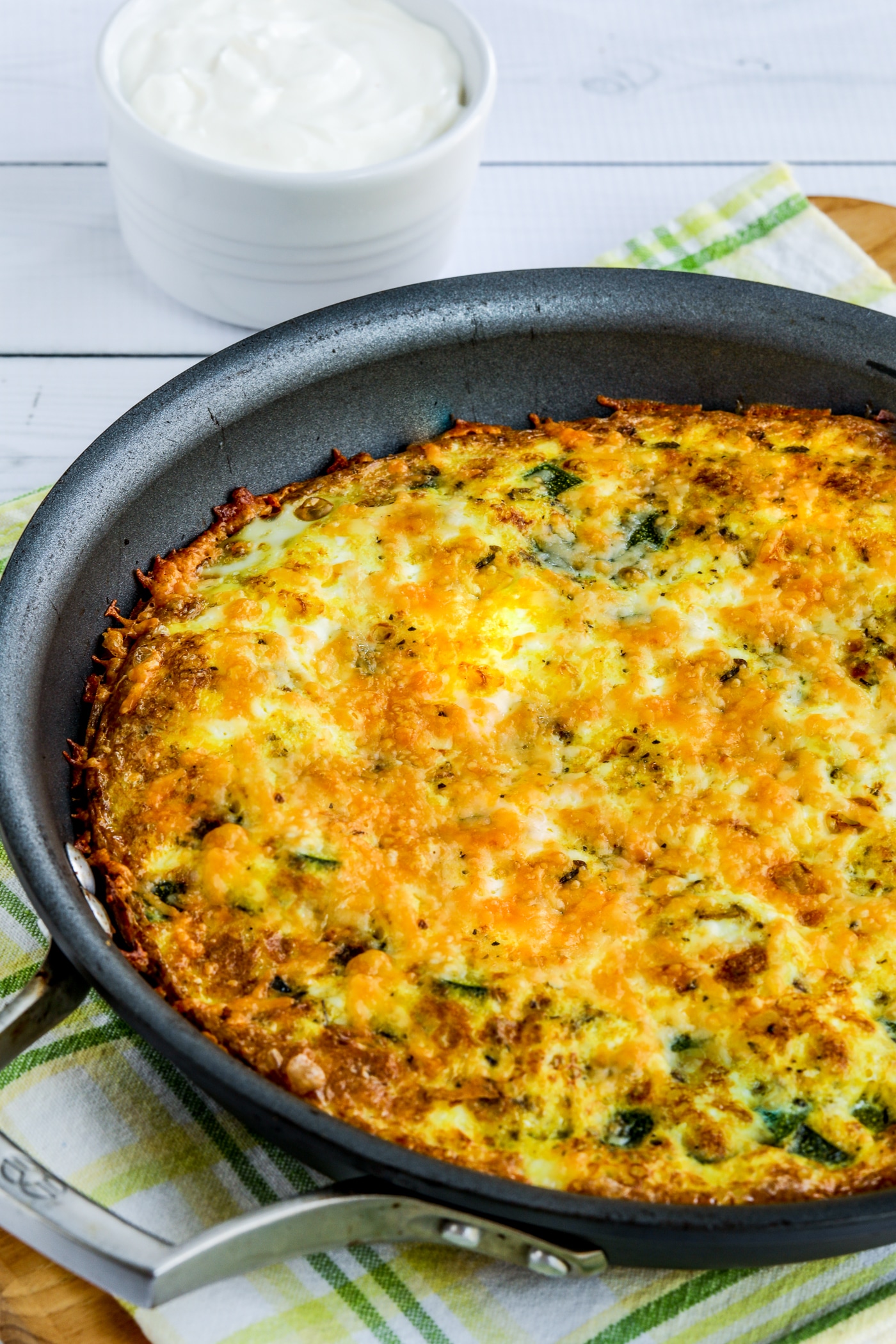 Close-up of a zucchini frittata displayed in a frittata pan with sour cream on the side