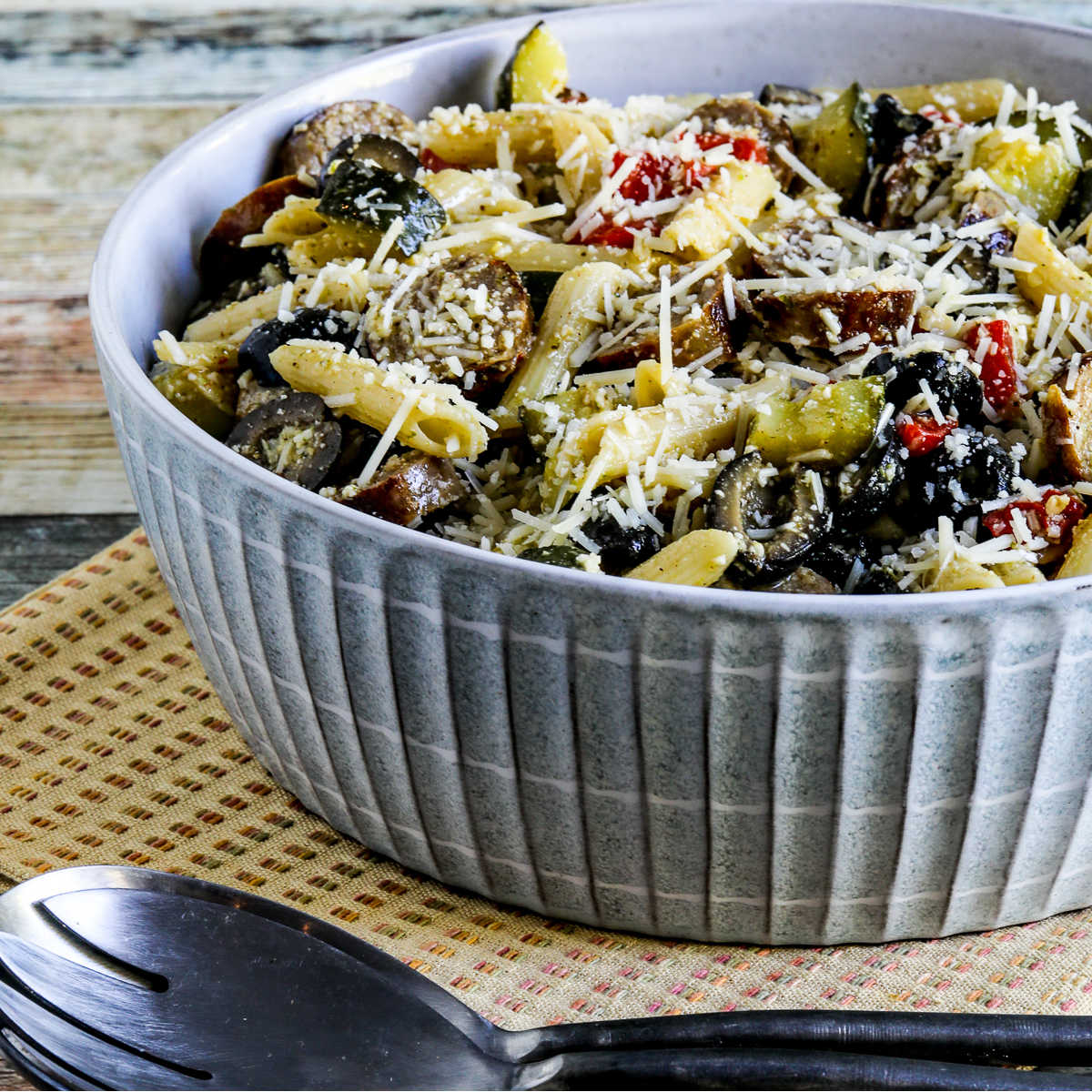 Pasta Salad with Sausage, Zucchini, Olives, and Peppers in serving bowl with forks and napkin