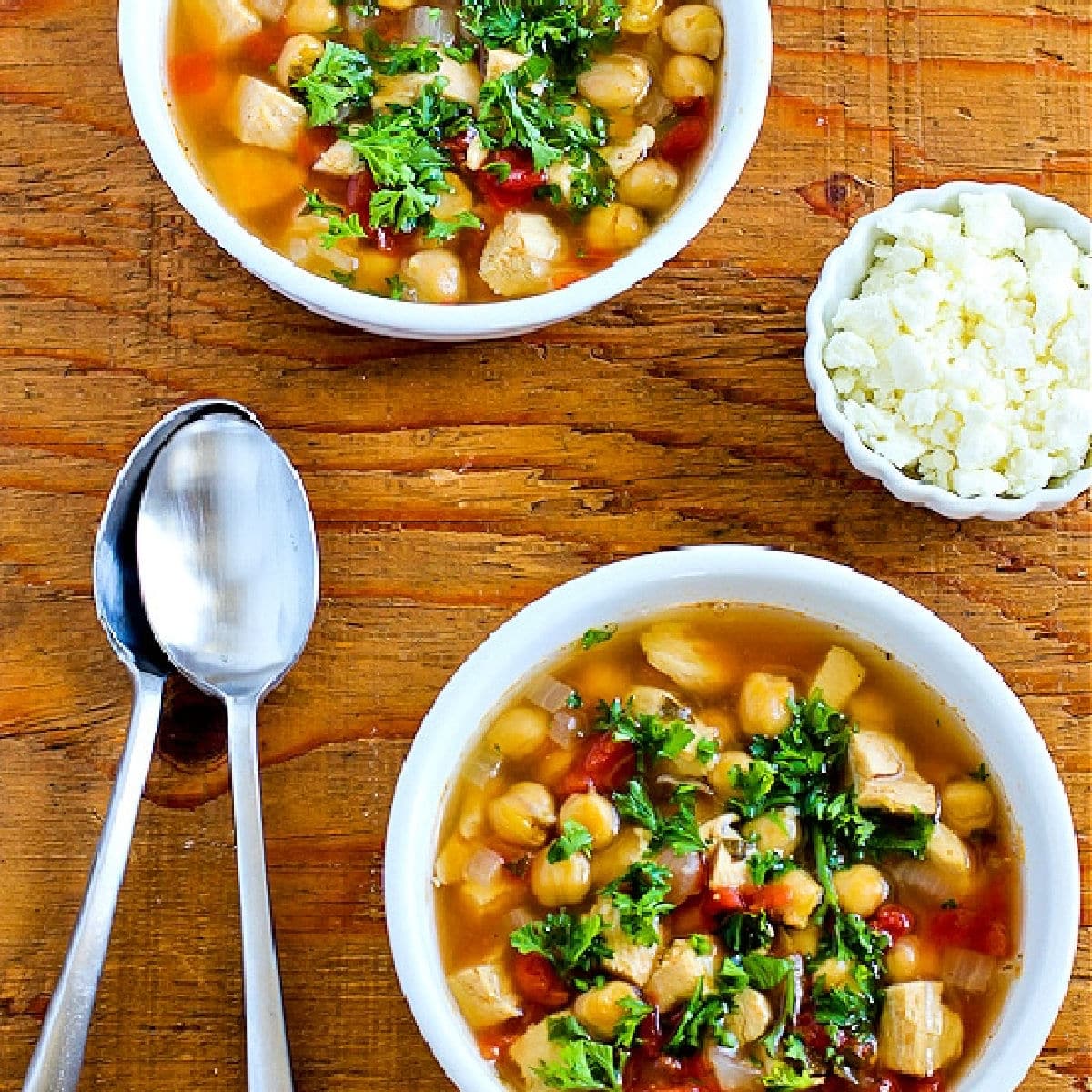 Square image for Chicken and Chickpea Soup shown in two bowls, with Feta on the side.