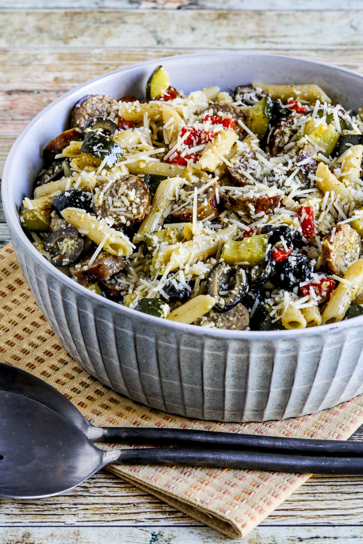 Pasta salad with sausage, zucchini, olives and peppers shown in a serving bowl on a napkin.