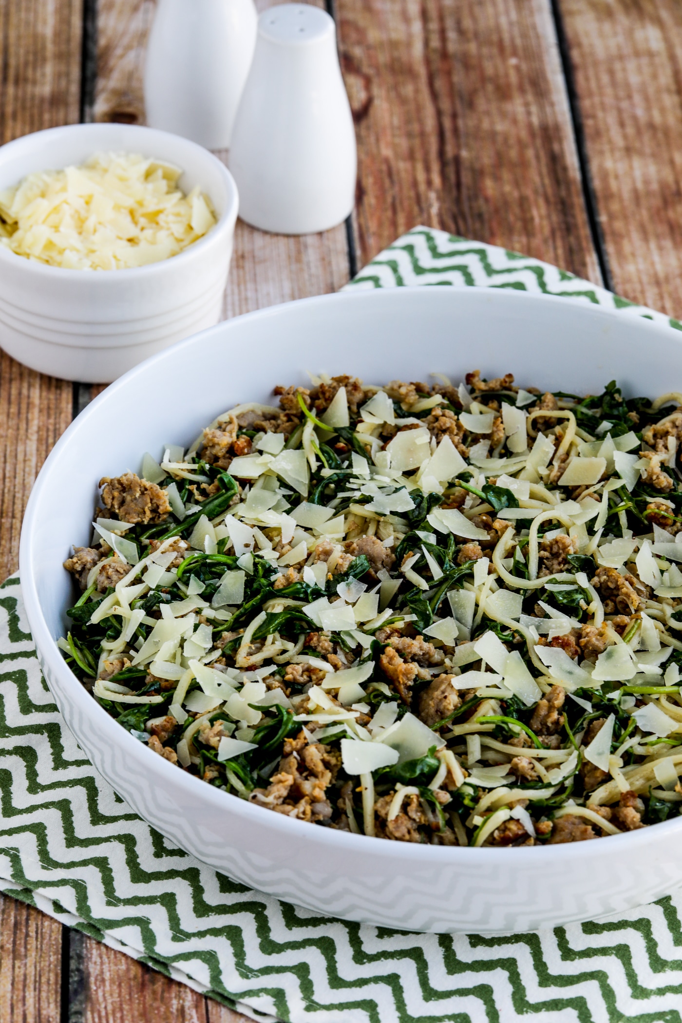 spaghetti with Italian sausage and arugula shown in serving bowl with Parmesan cheese