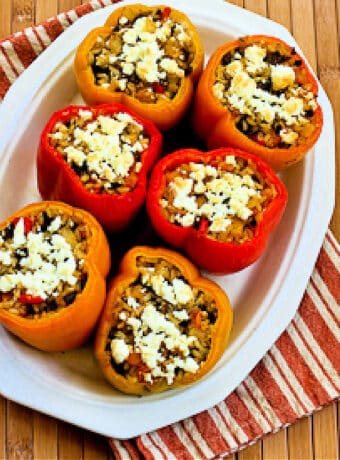 Vegetarian Stuffed Peppers (with mushrooms and Feta) shown on serving plate with red, yellow, and orange peppers.