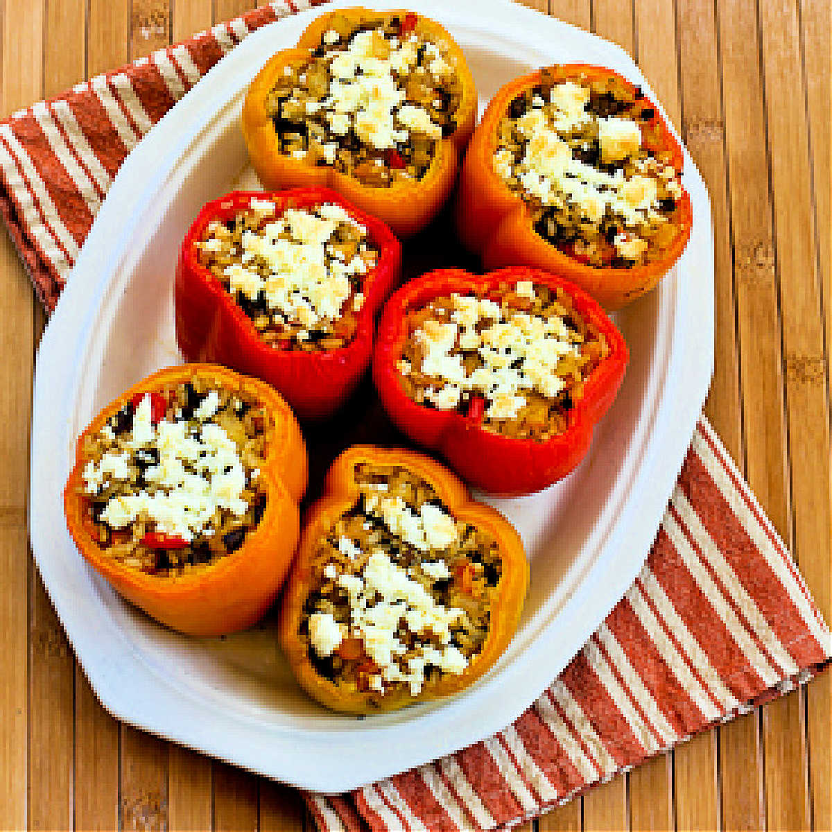 Vegetarian Stuffed Peppers (with mushrooms and Feta) shown on serving plate with red, yellow, and orange peppers.