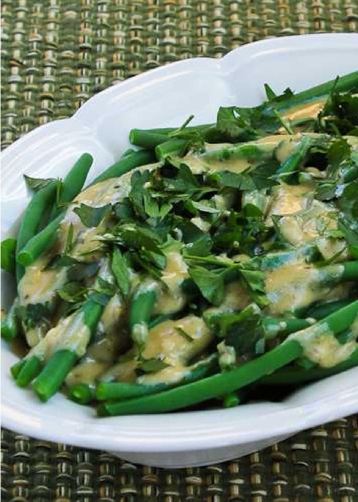 Vertical image of green beans with tahini and lemon in a serving bowl