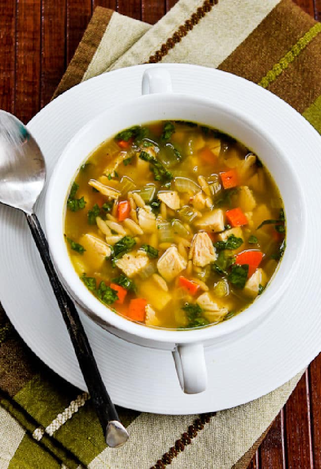 Cropped image of Slow Cooker Turkey Soup in bowl with plate and spoon.