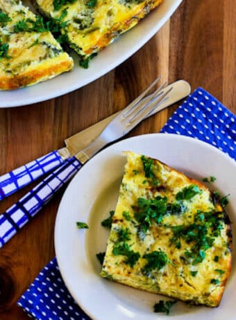 Slow Cooker Broccoli Casserole with Three Cheeses, square image showing one serving on plate and slow cooker in back.