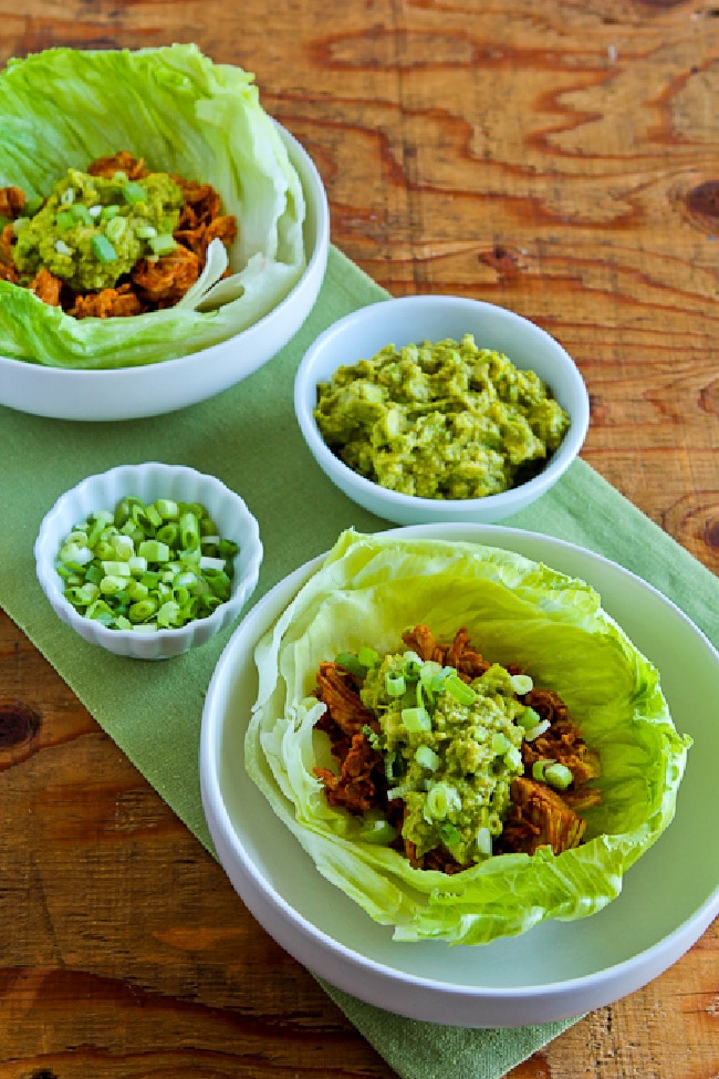 Slow Cooker Barbecue Chicken shown in lettuce cups with guacamole and green onions for topping.