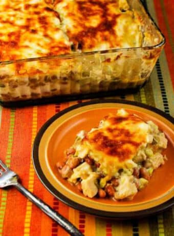 Square image for Mexican Chicken Casserole with Pinto Beans shown with one serving on plate and baking dish in back.