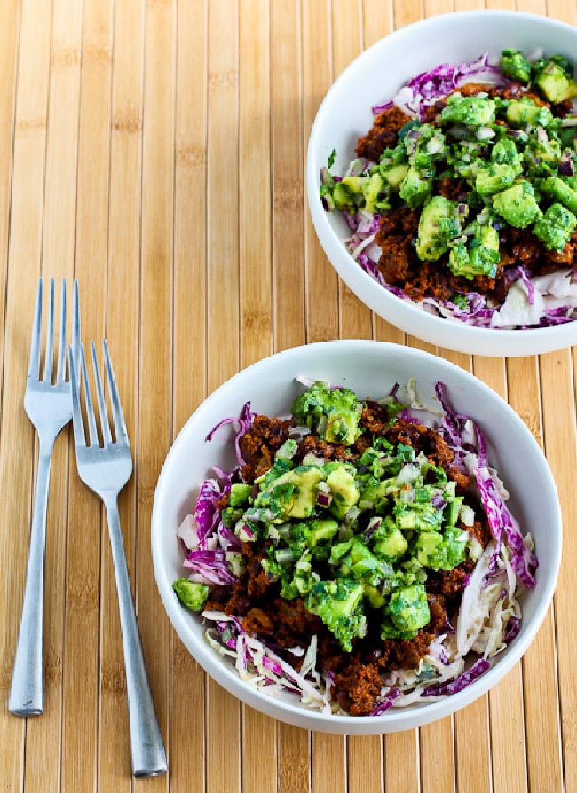 Ground Turkey Taco Bowls with ingredients shown in two cabbage bowls topped with avocado salsa