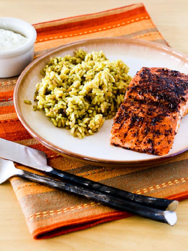 Roasted salmon in olive oil with sumac and tzatziki sauce on a serving plate.