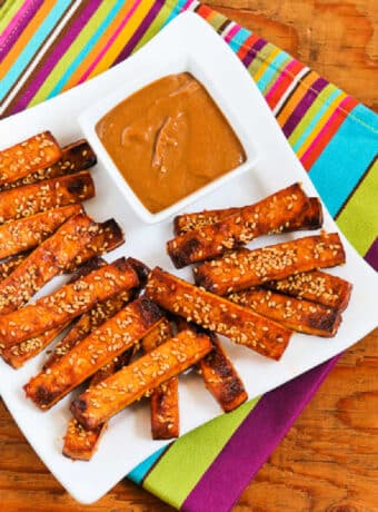 Baked Sesame Tofu Sticks shown on serving plate placed on colorful napkin.