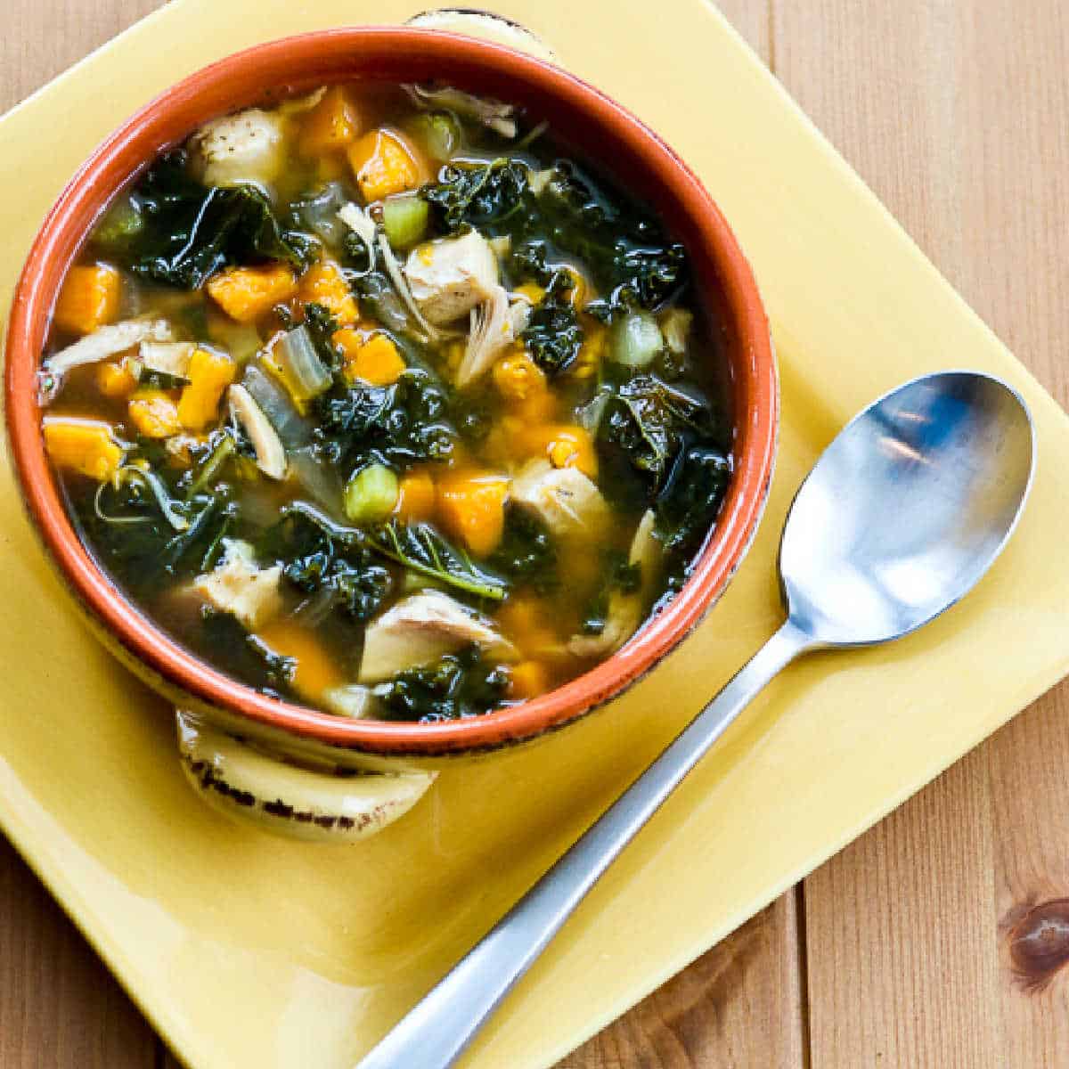 Slow Cooker Turkey Soup with Kale and Sweet Potatoes shown in bowl on yellow plate.