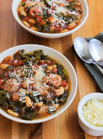 Square image for Slow Cooker Sausage Stew shown in two serving bowl with spoons and Parmesan cheese on the side.