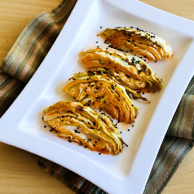 A square picture of roasted cabbage with lemon and sriracha in a serving dish with black sesame seeds