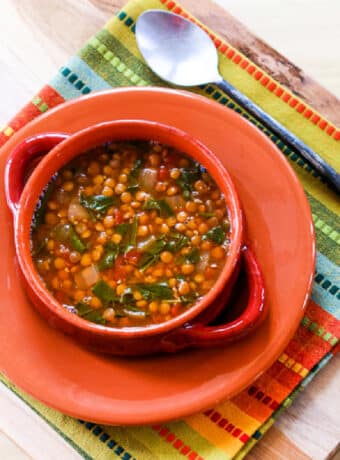 Vegetarian Lentil Spinach Soup shown in orange bowl with plate and colorful napkin.