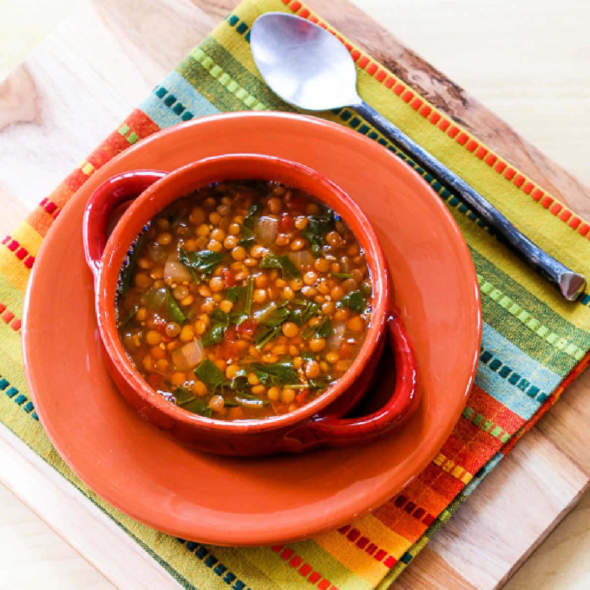 Square image of Vegetarian Lentil Soup with Spinach shown in bowl on orange plate.