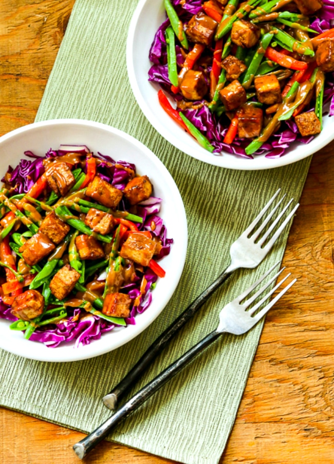 two cabbage bowls with tofu cubes, veggies, and peanut sauce