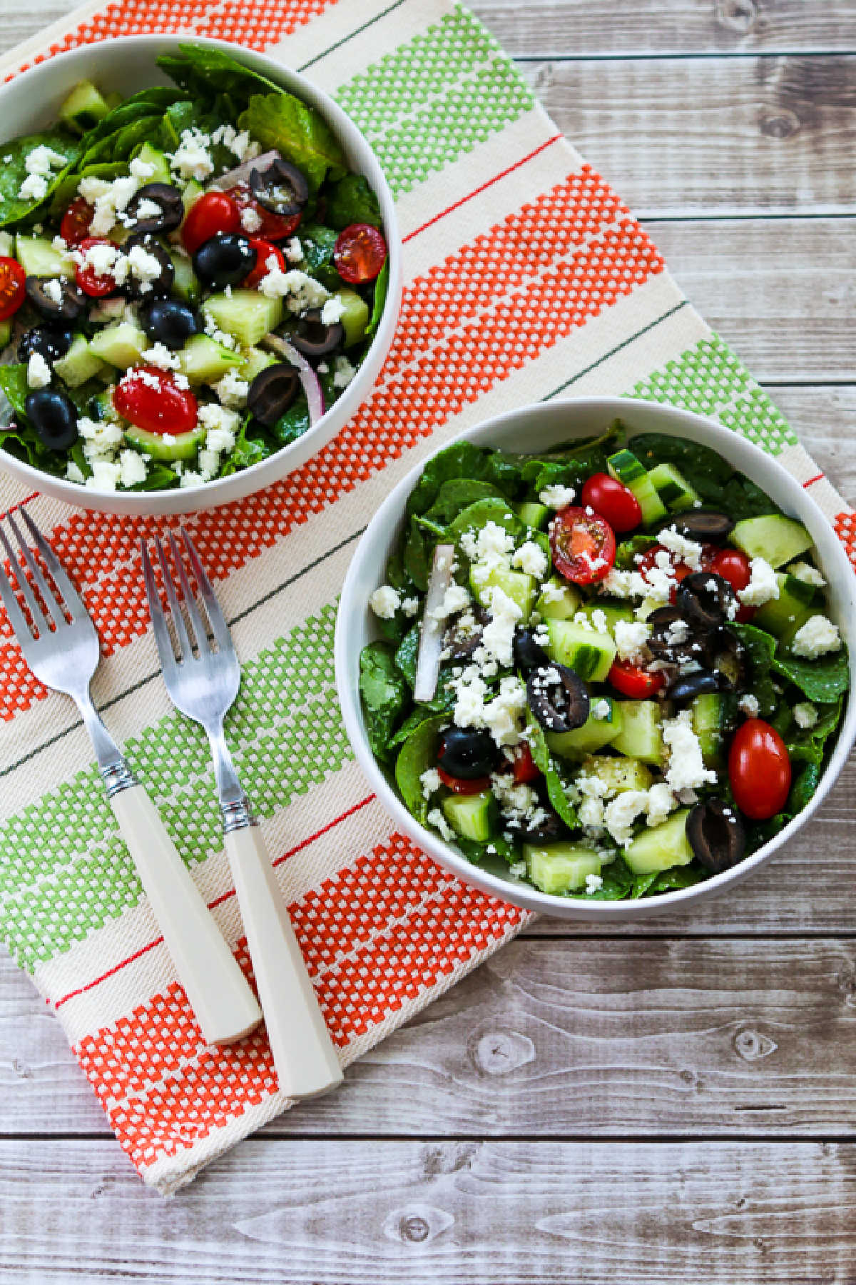 Kale Greek Salad in two serving bowls on green-red striped napkin