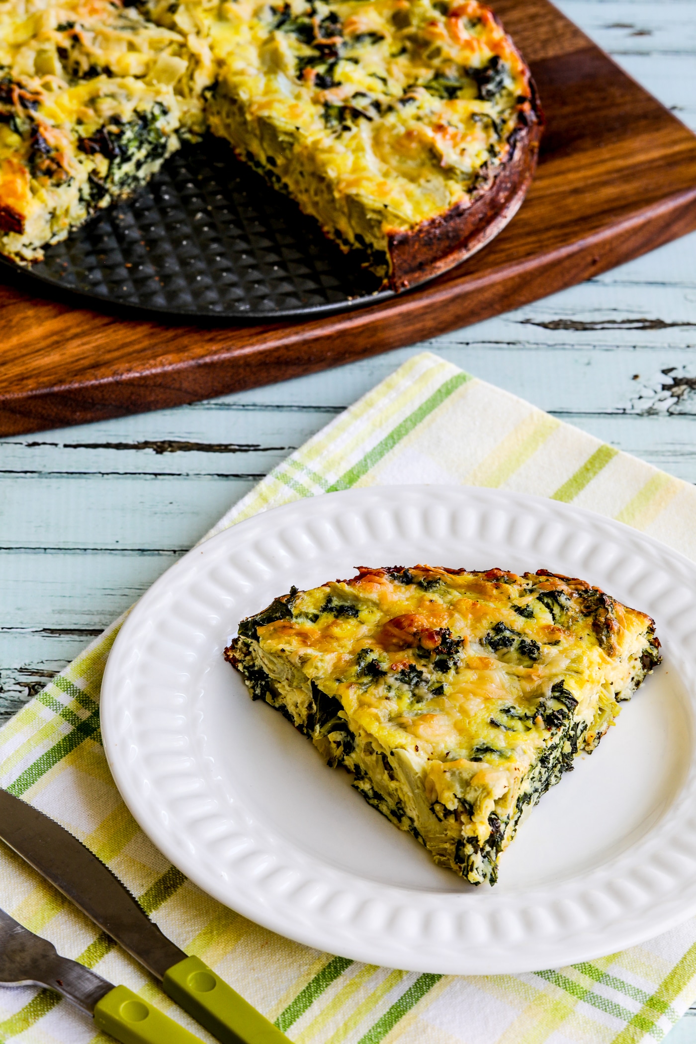 Artichoke, Kale, and Ricotta Pie finished pie with one slice on plate and the rest on the back on a cutting board