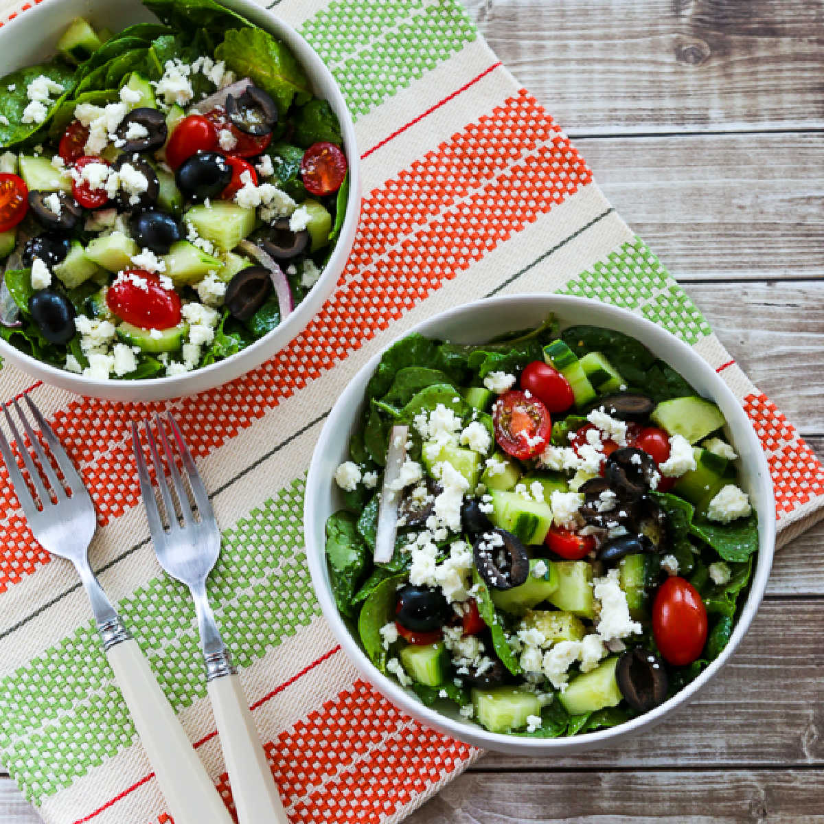 Kale Greek Salad in two bowls with forks on striped napkin.