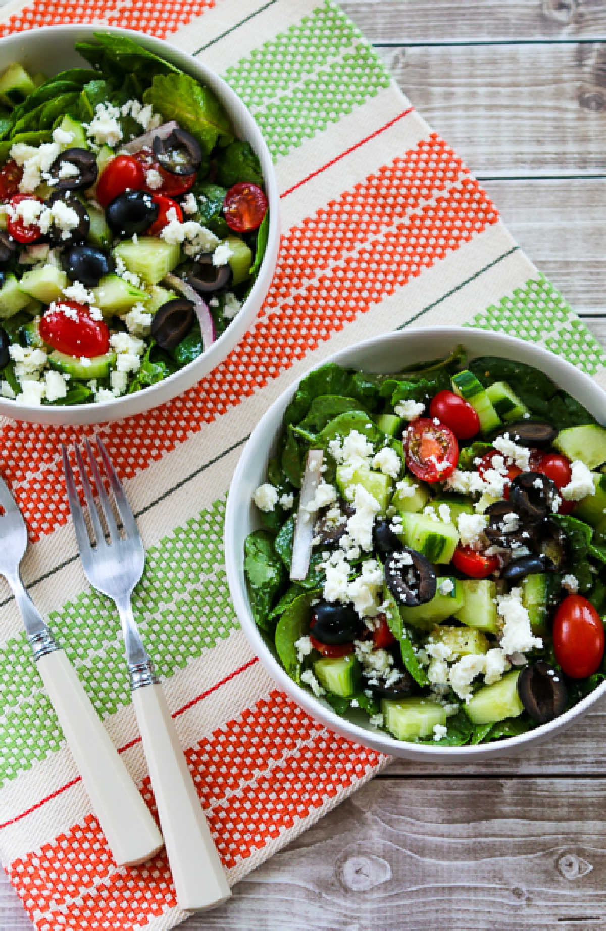 Kale Greek Salad shown in two bowls with forks and napkin