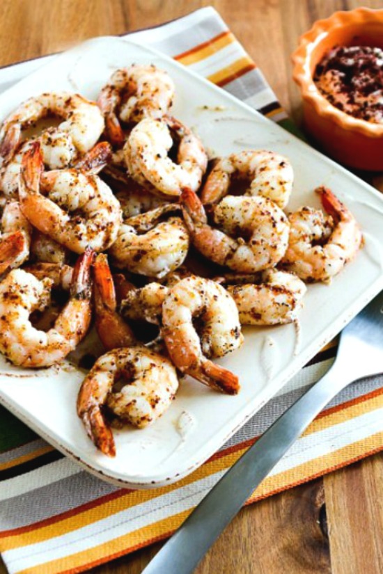 spicy baked shrimp on serving plate with napkin, fork, and sauce in background