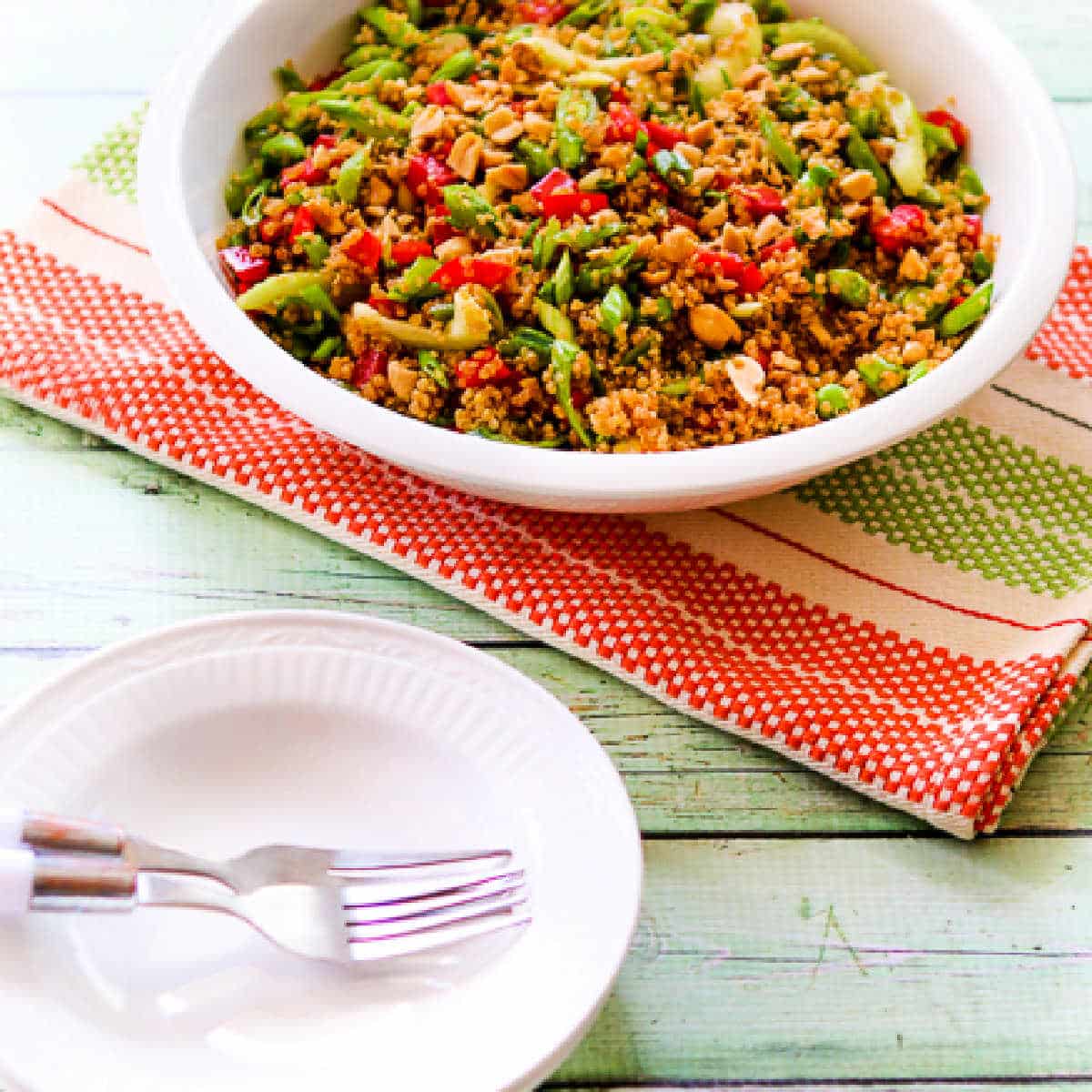 Square image for Asian Quinoa Salad shown in serving bowl with napkin, bowls, and plates.