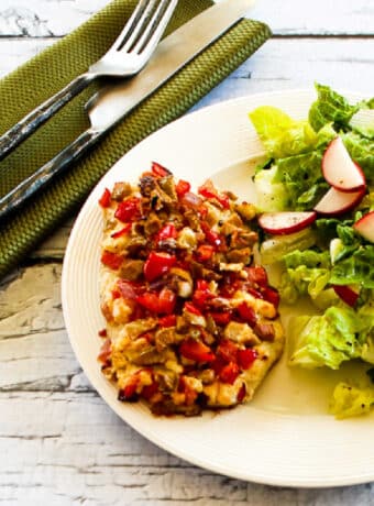 Square image of Baked White Fish with Onions, Peppers, Olives, and Feta shown on serving plate with salad.