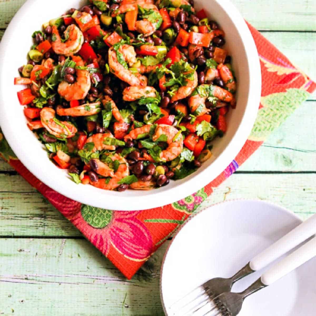 Square image of Shrimp and Black Bean Salad in bowl with plates, forks.