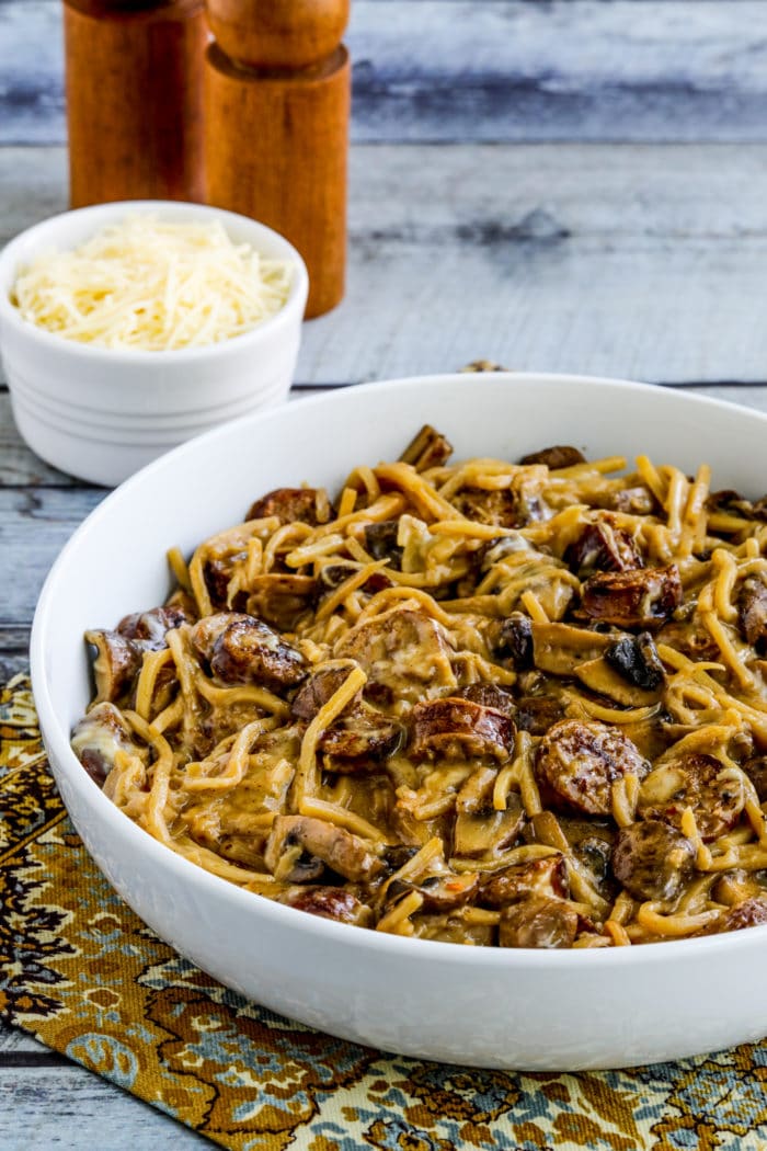 Low-Carb Pasta with Sausage and Mushrooms in serving bowl with Parmesan in background