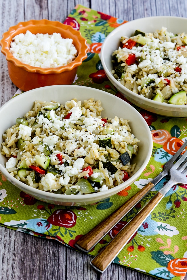 Slow Cooker Brown Rice with Veggies and Feta shown in two serving bowl with extra feta on the side