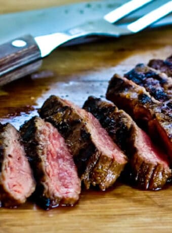 Grilled Cuban Flank Steak shown on cutting board with carving fork and knife