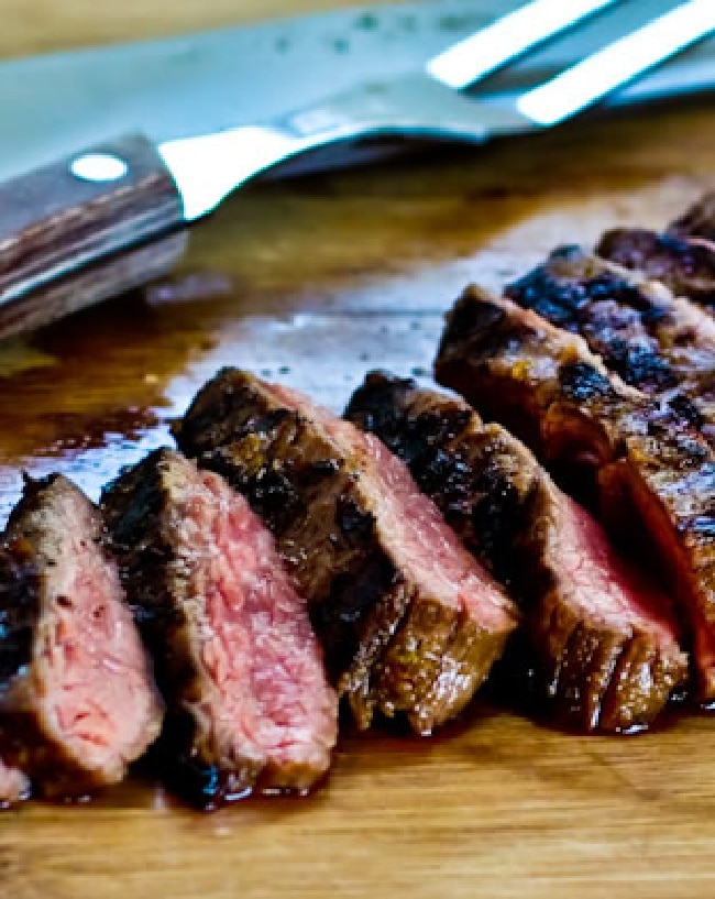 Cuban blank steak sliced on cutting board, with meat fork in background