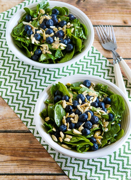 Power Greens Salad with Blueberries in two serving bowls with forks and napkin