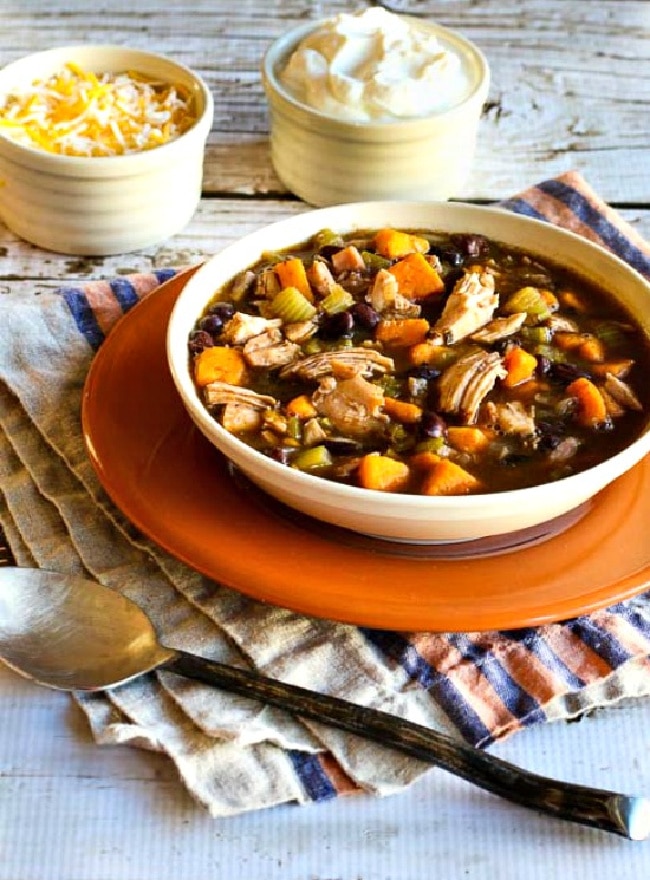 Turkey, Sweet Potato, and Black Bean Soup soup shown in bowl with spoon and toppings.