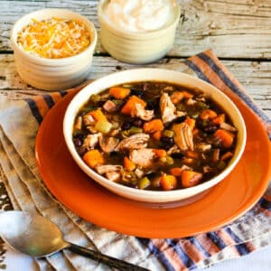 Square image for Turkey, Sweet Potato, and Black Bean Soup, shown in bowl on orange plate.