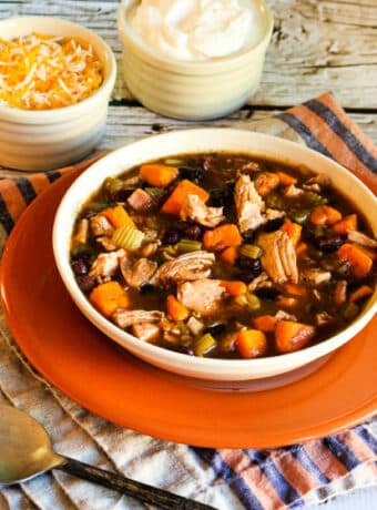 Square image for Turkey, Sweet Potato, and Black Bean Soup, shown in bowl on orange plate.