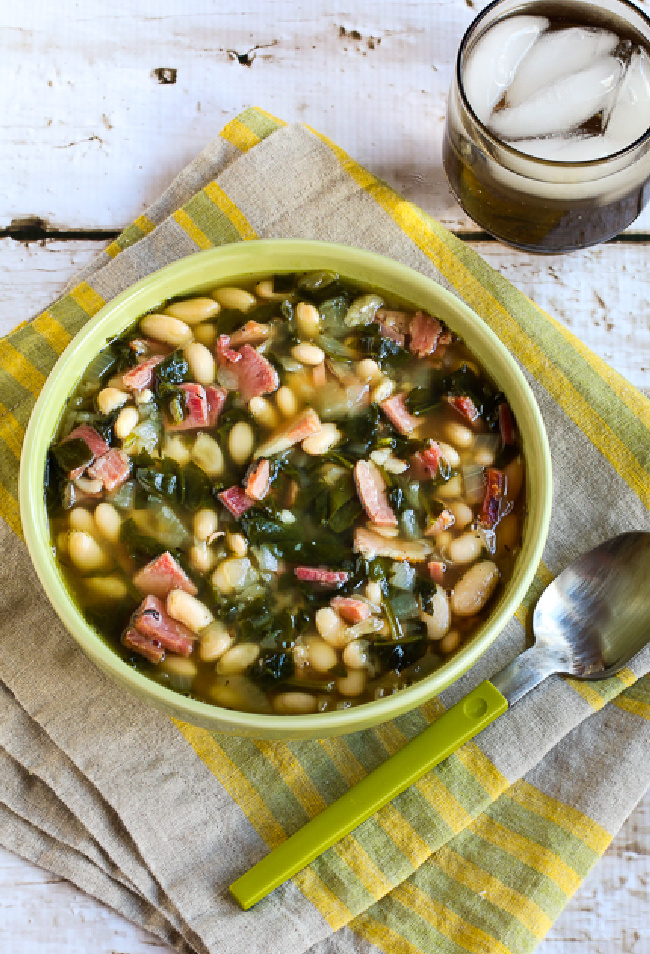 Slow Cooker Bean Soup with Ham, Spinach, and Thyme shown in bowl with spoon and drink in background