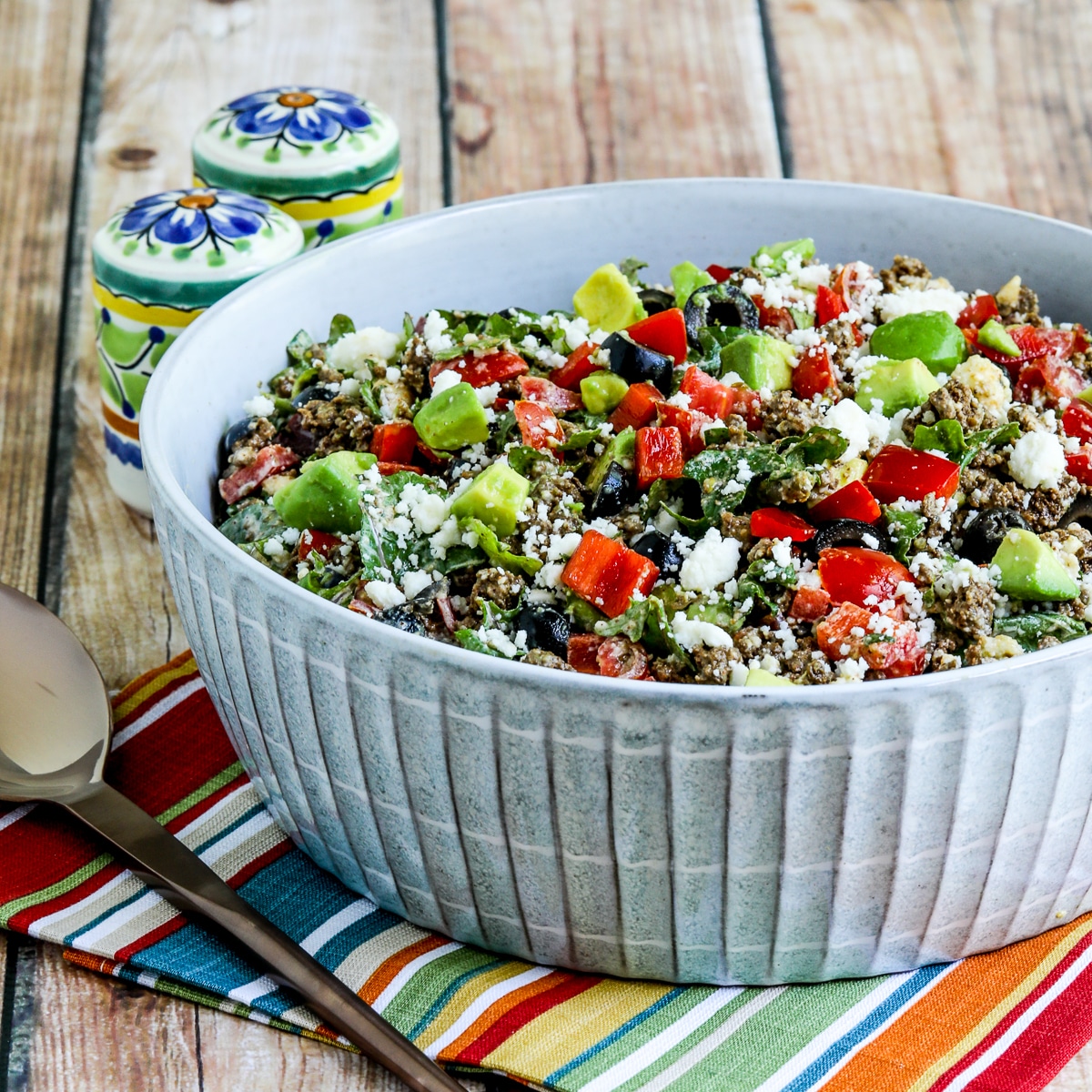Square image of ground beef taco salad with kale, tomato and avocado in a serving bowl.