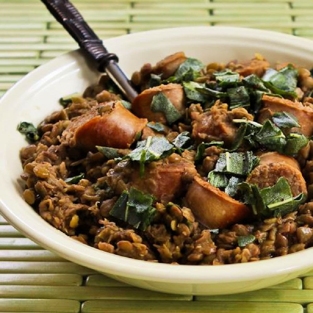 Sausage and Lentils with Fried Sage shown in serving bowl with fork.