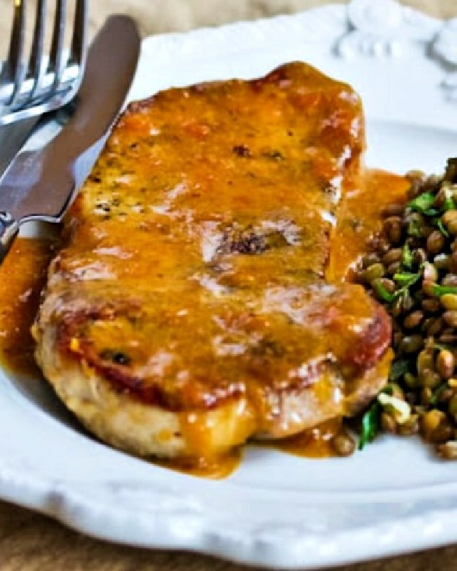 Apricot Glazed Pork chops shown on serving plate with knife-fork and lentils on the side.