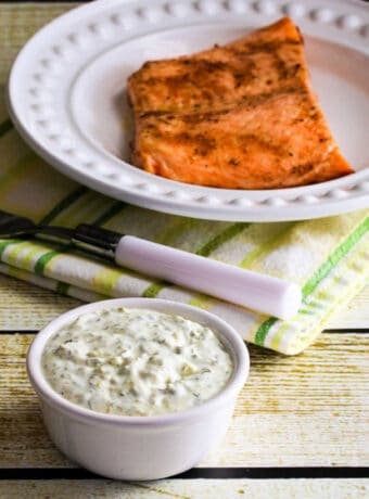 Square image of Double-Dill Homemade Tartar Sauce with tartar sauce in bowl and cooked salmon on plate in background