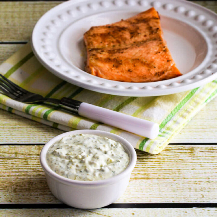 Square image of Double-Dill Homemade Tartar Sauce with tartar sauce in bowl and cooked salmon on plate in background