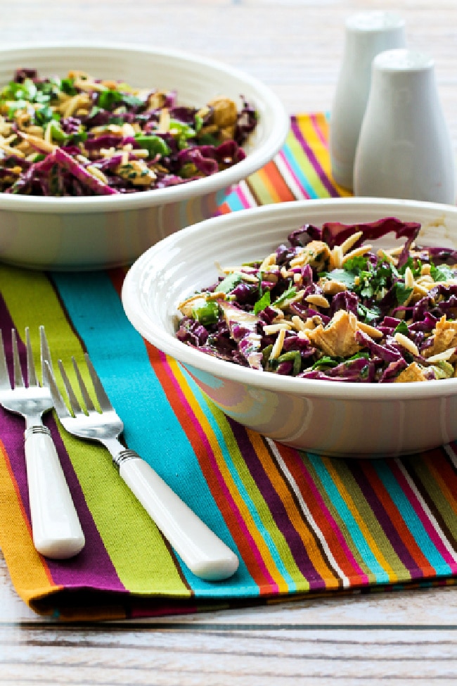 Asian Red Cabbage Salad with Chicken shown in two bowls with forks, salt, and pepper.