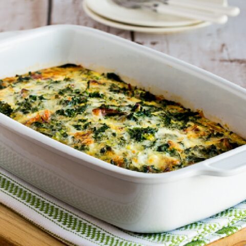 Kale, Bacon, and Cheese Breakfast Casserole in baking dish with plates-forks in background
