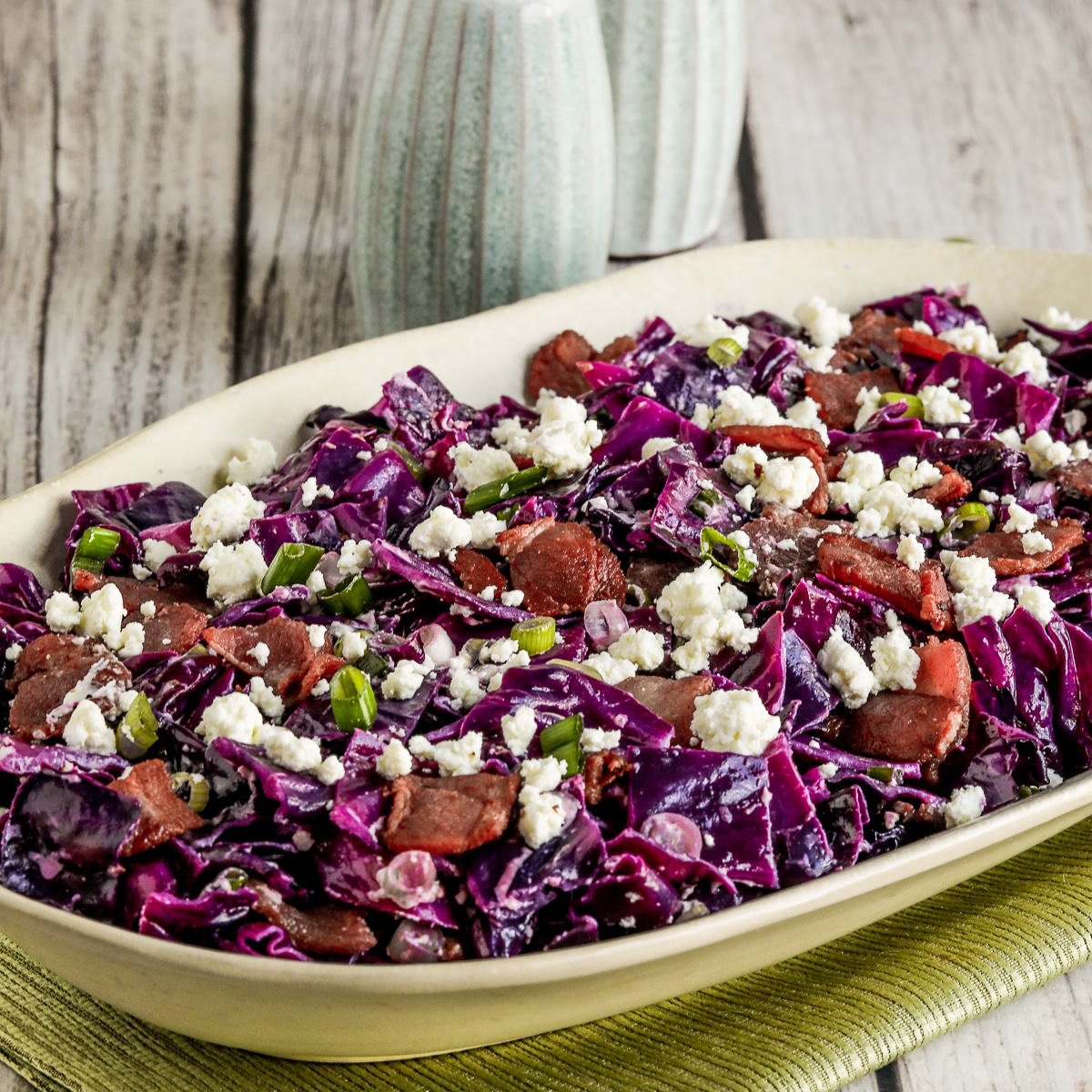 Square image of red cabbage salad with bacon and goat cheese displayed on a serving plate